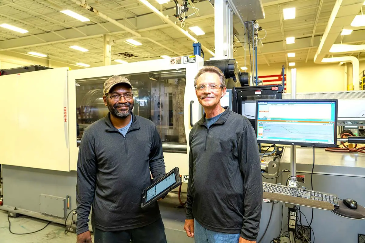 Two Rosti Staff in front of Plastic injection molding machine