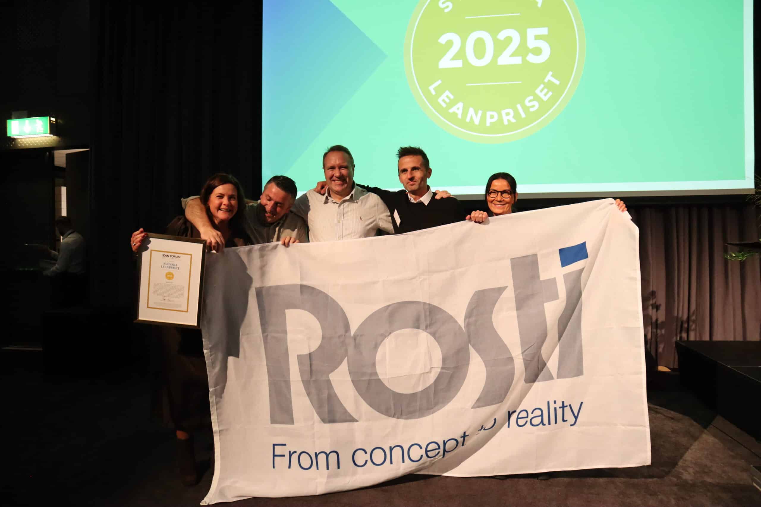 Rosti GP staff with a Rosti Flag celebrating the Lean award 2025.